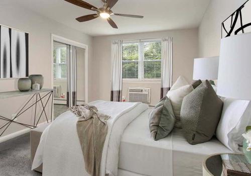 Bed with a ceiling fan and an open window at Gardens of Mt. Airy apartments for rent